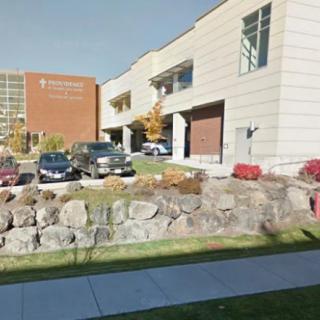 A modern building with a parking lot and several cars, surrounded by rock landscaping and a sidewalk.
