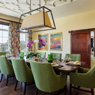 A beautifully designed dining room featuring green upholstered chairs, a modern hanging light fixture, and vibrant artwork on the wall.