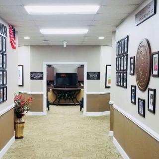 A well-lit office hallway adorned with framed photos and an American flag, leading to a meeting room.