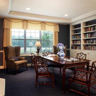 A cozy library with bookshelves, a wooden table, and chairs by a large window.