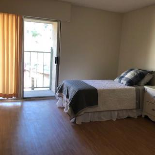 A minimalist bedroom with a double bed, adjacent to a sliding door leading to a balcony.