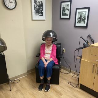 A person sitting under a vintage hair dryer in a salon.