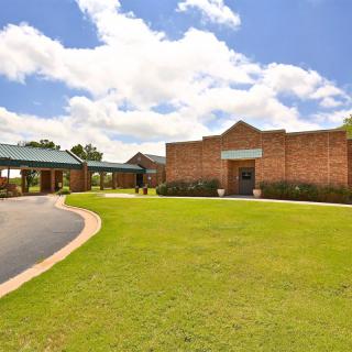 A brick school building with a well-maintained lawn and driveway under a blue sky with white clouds.