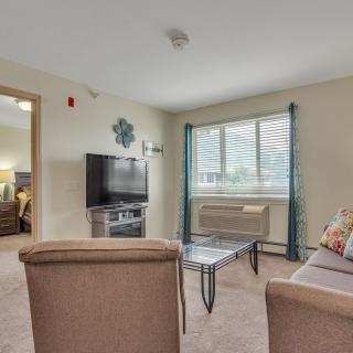 A cozy living room with a TV, seating area, and large window.