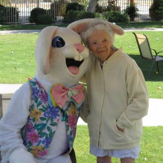 An elderly woman poses with a person in an Easter Bunny costume at a park.