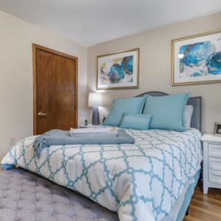 A cozy bedroom with a neatly made bed, decorated with blue and white bedding and complemented by artwork on the walls.