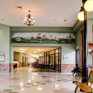 A spacious hallway with a mural, chandeliers, and benches.