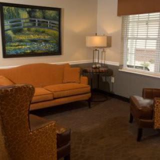 A cozy living room with an orange sofa, armchairs, a lamp, and a painting on the wall.