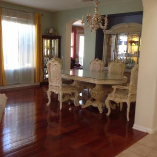 An elegant dining room with ornate furniture and a chandelier, featuring polished wood flooring.