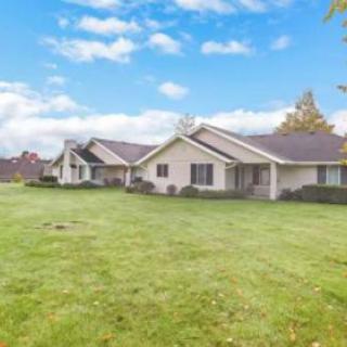 A suburban house with a large grassy lawn under a blue sky with clouds.