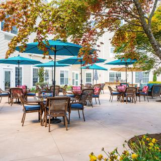 A charming outdoor patio with tables, chairs, and umbrellas surrounded by lush greenery.