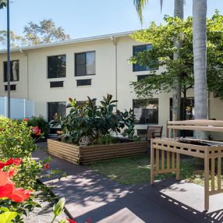 An apartment building with a well-maintained garden and lush greenery on a sunny day.