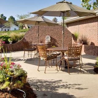 A sunny outdoor patio with tables, chairs, and umbrellas surrounded by a brick wall and vibrant flowers.