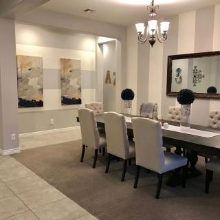 An elegant dining room with a long table, upholstered chairs, a chandelier, and modern artwork on the walls.