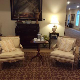 A cozy living room area with two cushioned chairs, a small wooden table between them, and a lamp providing warm light.