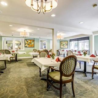 An elegantly decorated dining room with neatly arranged tables and chairs, featuring chandeliers and tasteful artwork.