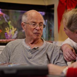 An elderly man and a woman are having a conversation indoors, near an aquarium.