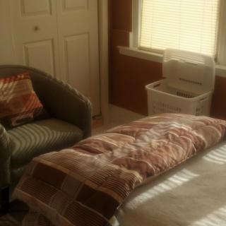 A cozy bedroom featuring a bed, an armchair, and a basket next to a window with blinds.