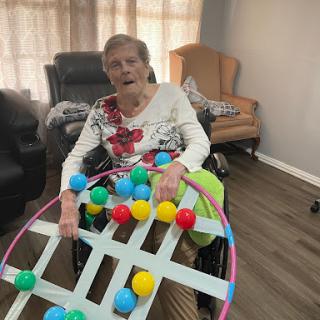 An elderly woman engaged in a colorful activity while sitting in her wheelchair.