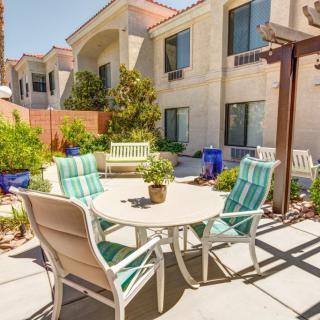 A sunny outdoor patio with a set of chairs and a table surrounded by garden plants and an adjacent building.
