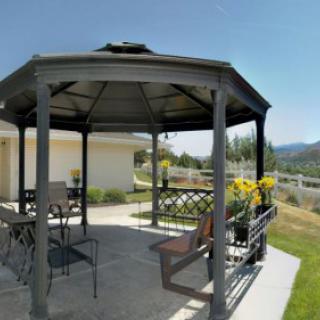 An outdoor gazebo with patio furniture on a sunny day, overlooking a garden and mountains.