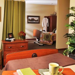 A cozy hospital room featuring a bed, bedside table with a coffee mug, and colorful curtains.