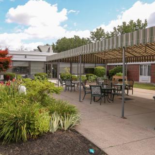 A well-furnished patio area with tables and chairs surrounded by lush greenery.
