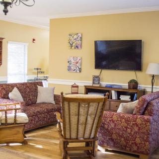 A cozy living room with a patterned sofa set, a wooden rocking chair, and a television mounted on the wall.