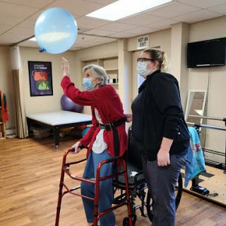 An elderly individual participates in a therapeutic exercise session while receiving assistance from a caregiver.