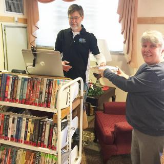 A librarian assists a patron using a mobile book cart indoors.