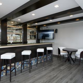 A modern bar area with sleek black and white decor, featuring a counter with stools and a television on the wall.