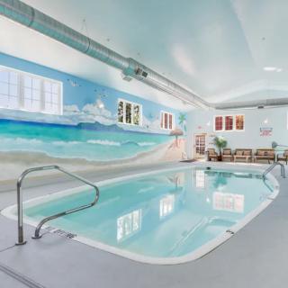 A serene indoor swimming pool with a vibrant beach-themed mural on the wall.