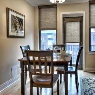 A cozy dining area featuring a wooden table and chairs with large windows adorned with blinds.