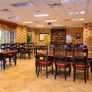 A spacious dining room with wooden tables and chairs arranged neatly, featuring warm lighting and decorative wall patterns.