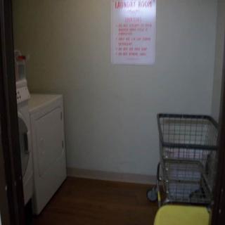 A small laundry room with a washing machine, a laundry cart, and a sign on the wall.