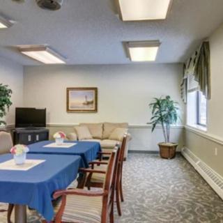 A small meeting room with blue tablecloths, chairs, a sofa, and potted plants.