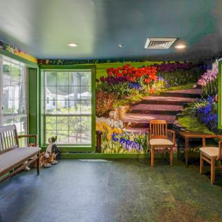 A room with a vibrant mural depicting a garden path, featuring seating and large windows.