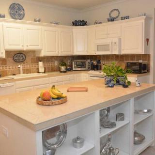 A modern kitchen with white cabinets and a countertop island, featuring a fruit basket and a small herb plant.