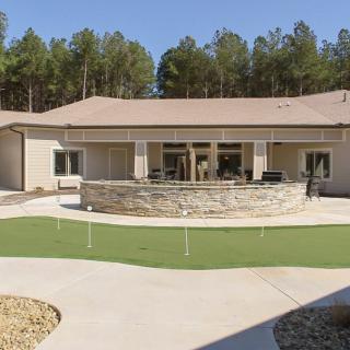 A modern house with a spacious backyard and patio area, surrounded by trees.