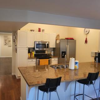 Modern kitchen with a large countertop and bar stools, featuring stainless steel appliances.