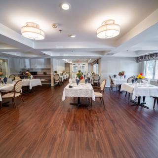 A well-lit dining area with elegantly set tables and chairs, featuring wooden flooring and modern decor.