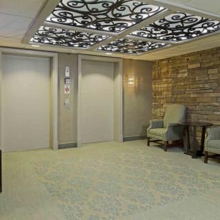 A modern elevator lobby featuring decorative ceilings, upholstered chairs, and a stone accent wall.