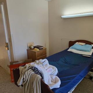 A simple bedroom featuring a single bed with unmade bedding and a bedside table.