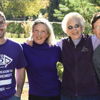 A cheerful group of four people posing together outdoors on a sunny day.