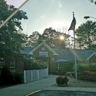 A peaceful morning view of a building with an American flag and surrounding greenery.