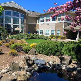 A scenic view of a modern building surrounded by lush gardens and a tranquil pond.