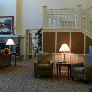 A cozy lobby interior featuring comfortable seating, warm lighting from lamps, and a staircase.