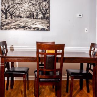 A dining area featuring a wooden table with four chairs and a framed landscape painting on the wall.