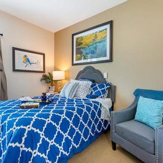 A cozy bedroom with blue patterned bedding and decorative pillows, complemented by wall art and a comfortable armchair.