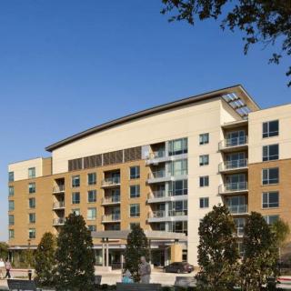 A modern apartment building with multiple floors and balconies, set against a clear blue sky.